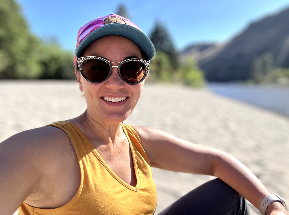 Chris sitting on a white sandy river beach in the sunshine. Looking directly into the camera and smiling.